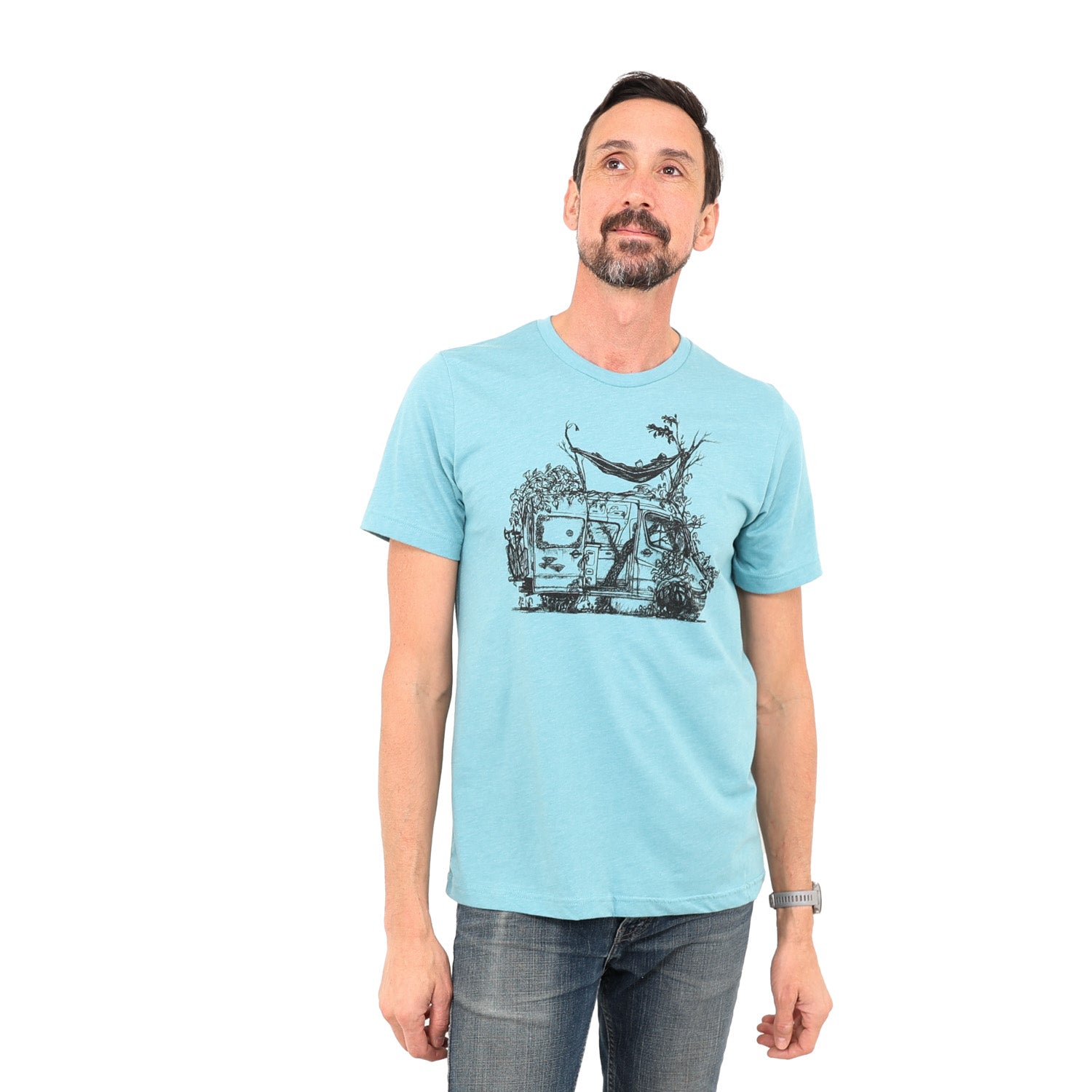 blue t-shirt with delapadated camper being taken back by earth. Tree growing right up the center of the van with person laying in hammock above sprinter like van