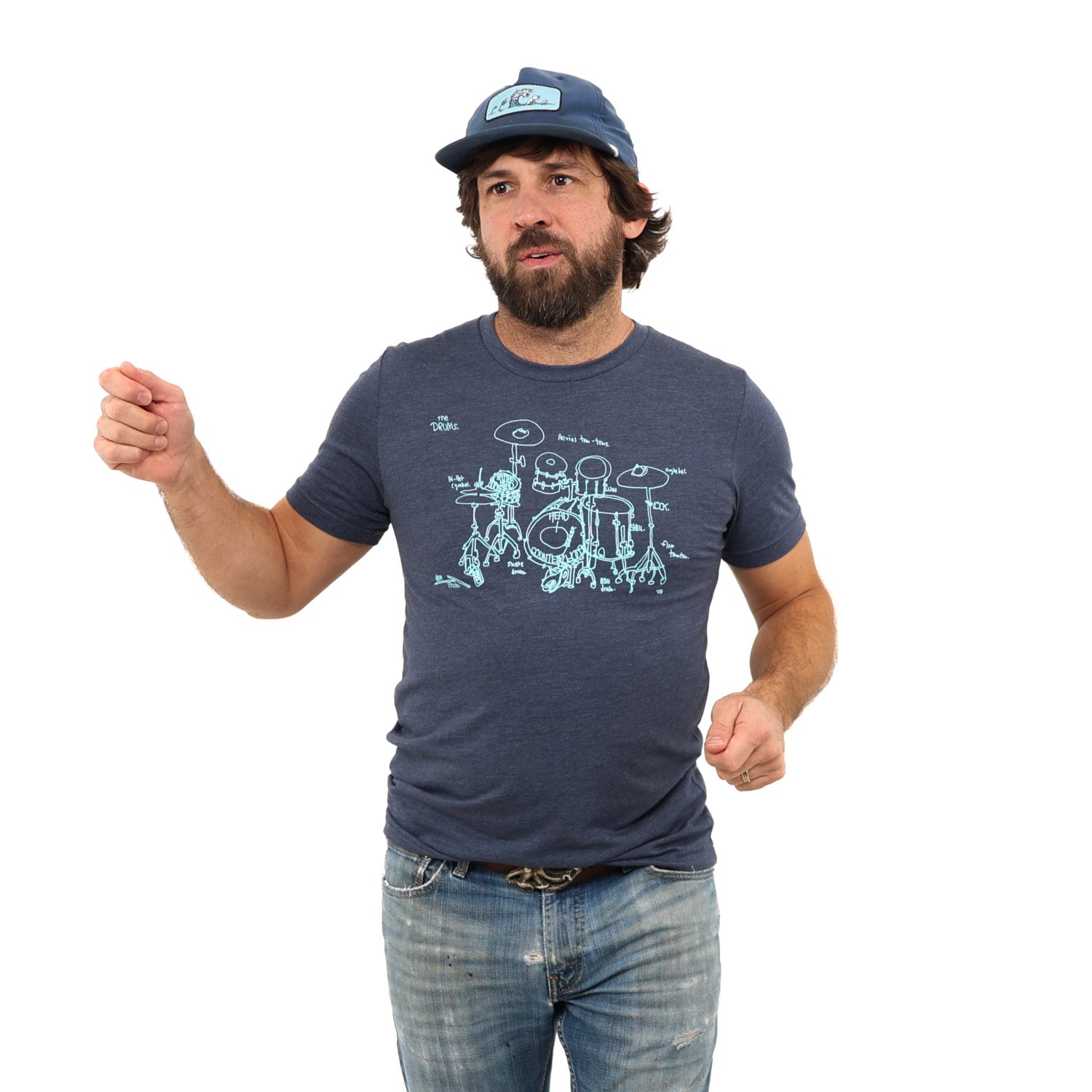 Man pretending to play drums while wearing a ball cap and a blue shirt with a drum set screen printed on it. White background.