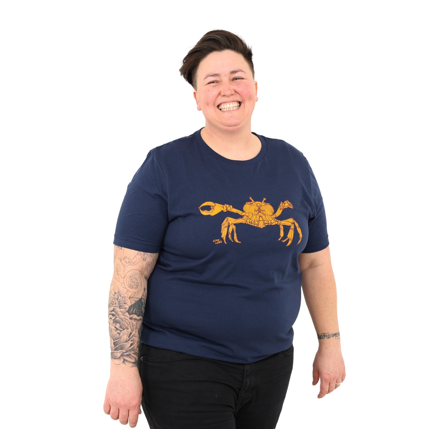girl with short hair smiling big while wearing black jeans and a blue t-shirt with a crab on it.