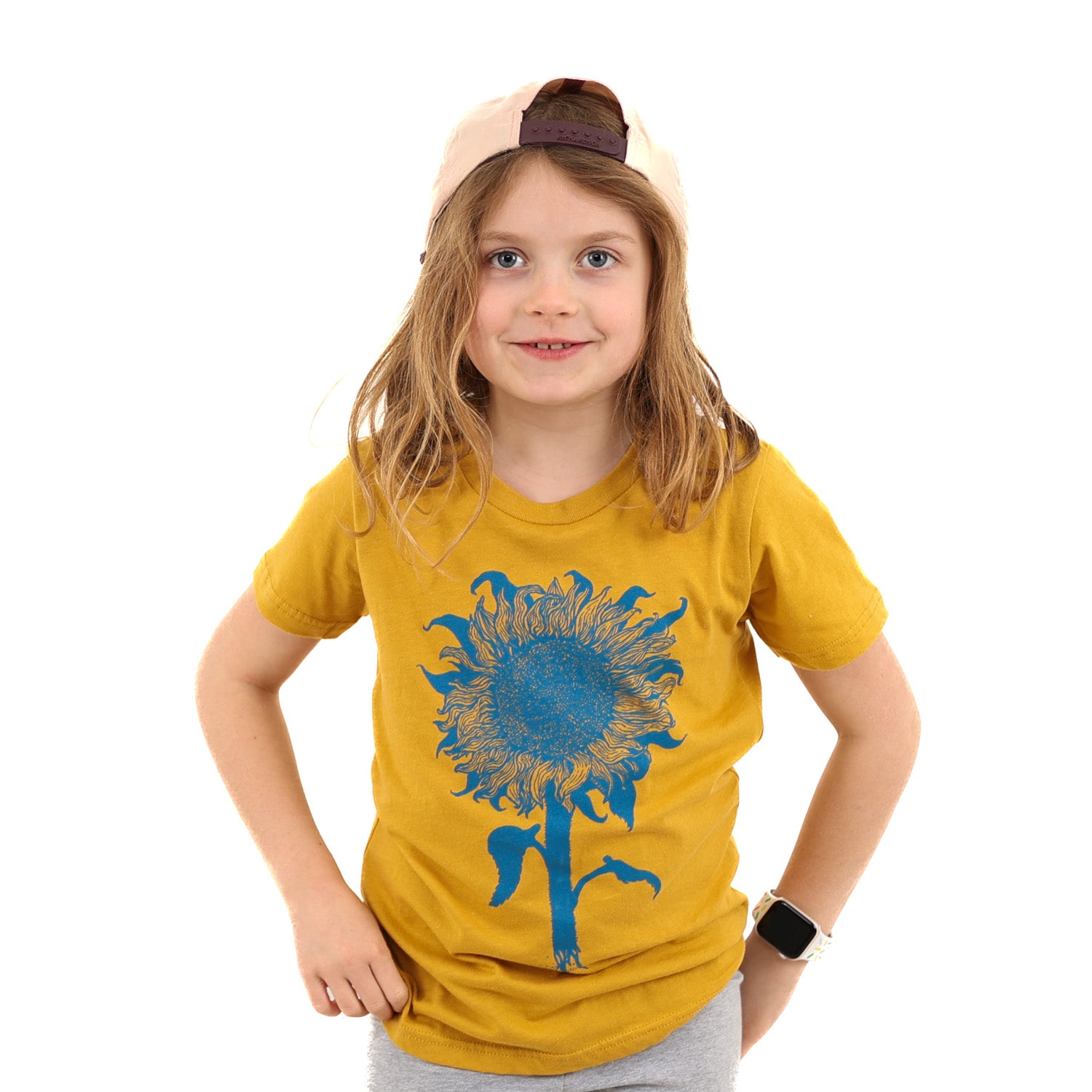 Little girl wearing a mustard colored t-shirt with light blue print of an intricate sunflower.