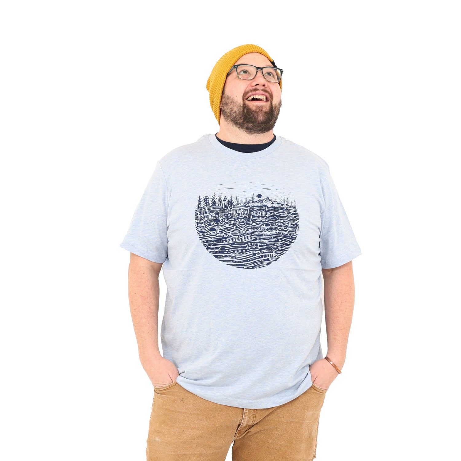 Man looking up while wearing heather light shirt with black ink print of the salish sea with mountains, trees, sky in the background.