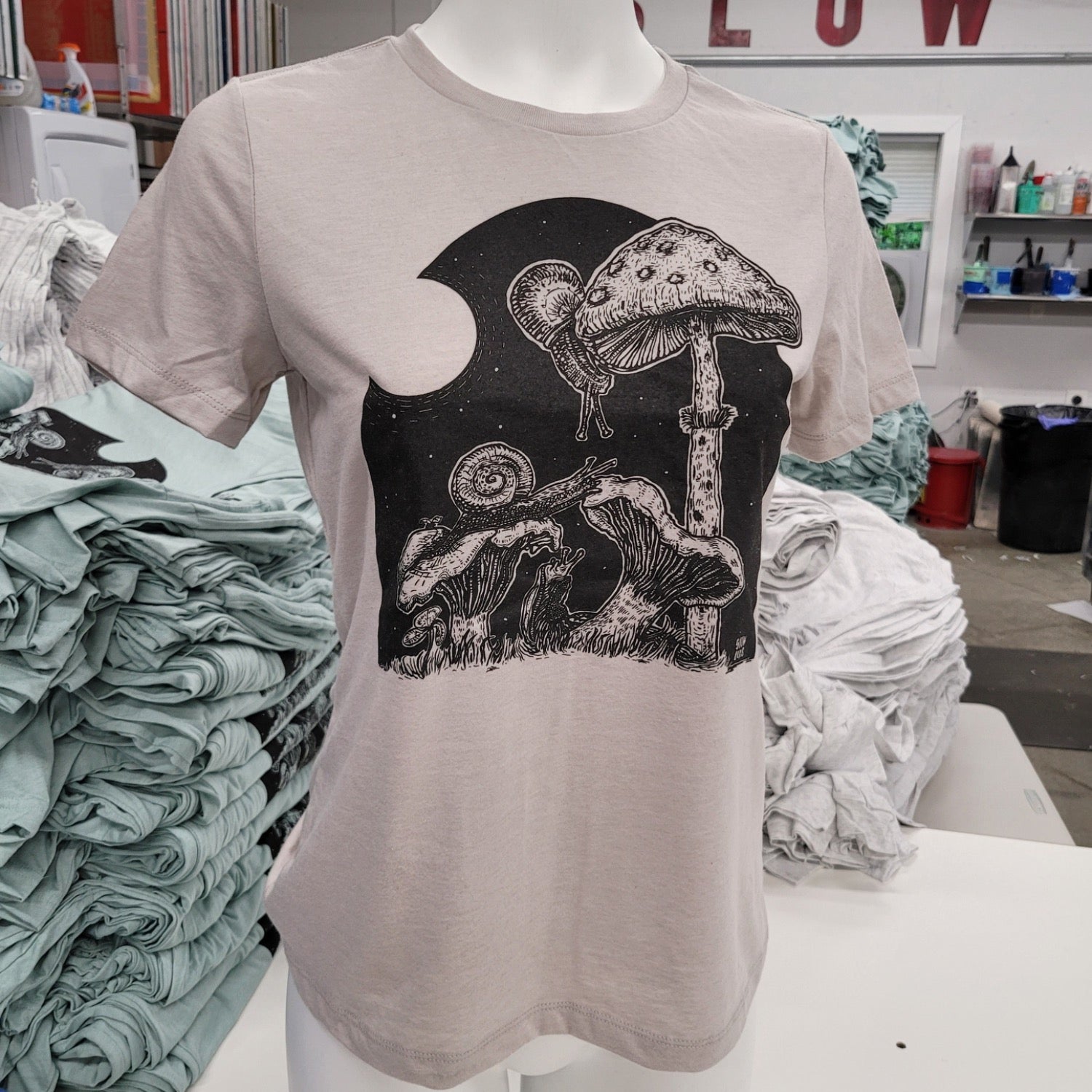 close up of off white t shirt with black in of mushrooms being eaten by snails.