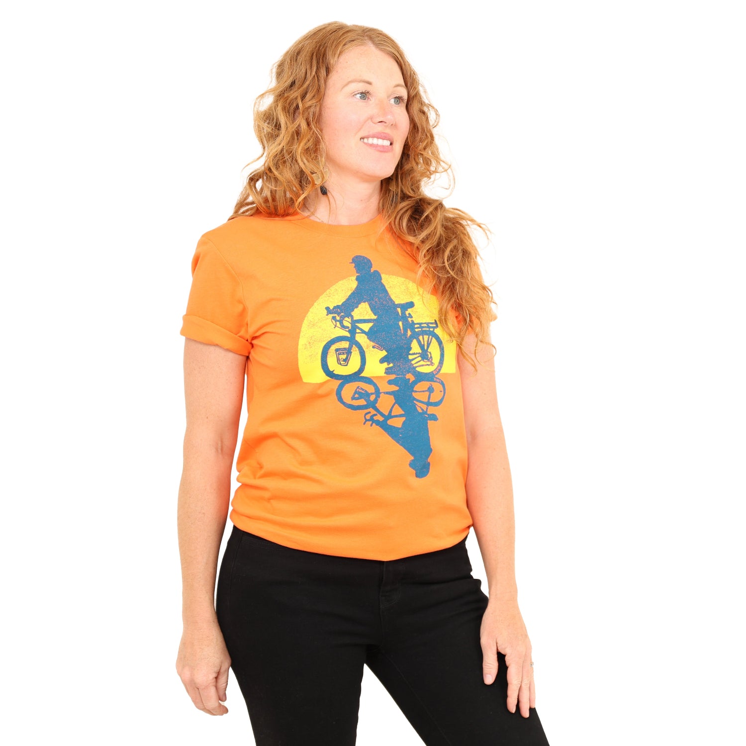 woman wearing orange t with print of a person riding bike with the sun setting in the back.