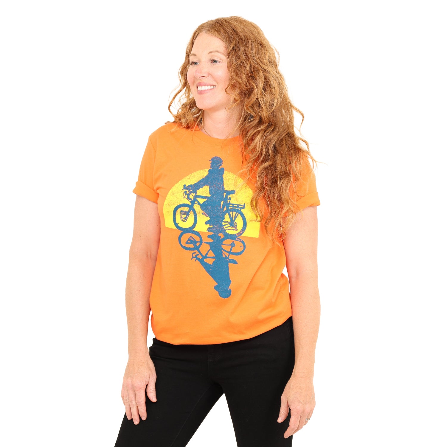 woman wearing orange t with print of a person riding bike with the sun setting in the back.
