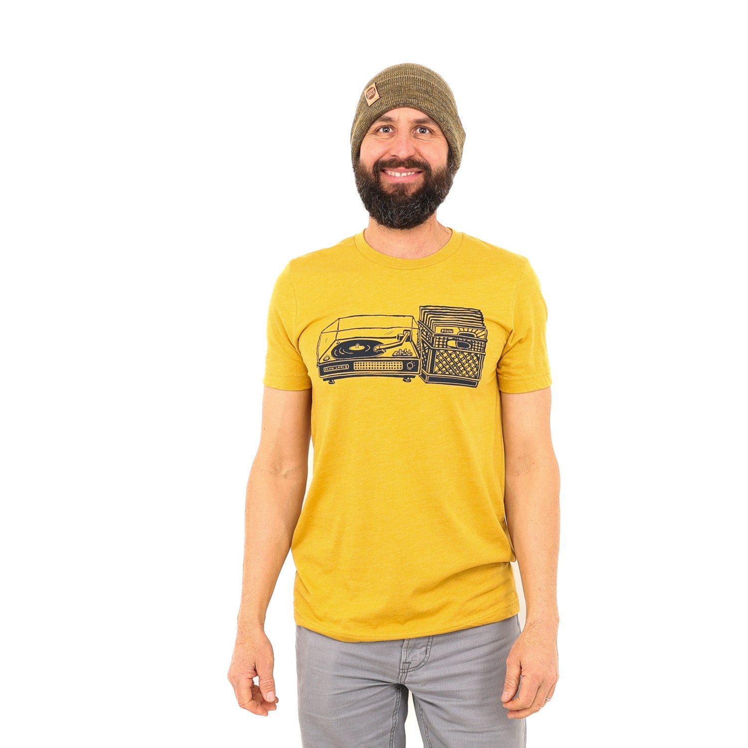 man wearing yellow shirt with black print of a record player with a milk crate full of records next to it.
