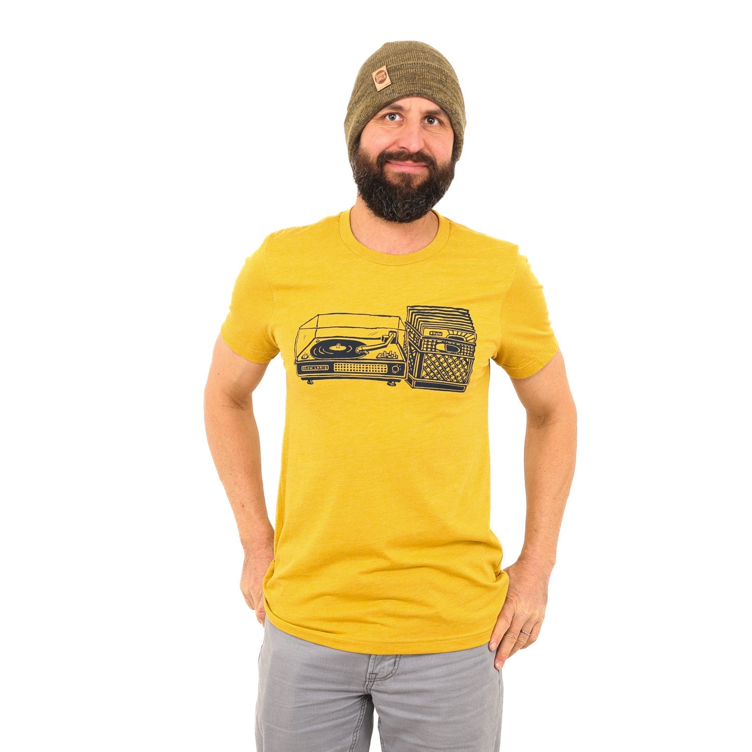 man wearing yellow shirt with black print of a record player with a milk crate full of records next to it.