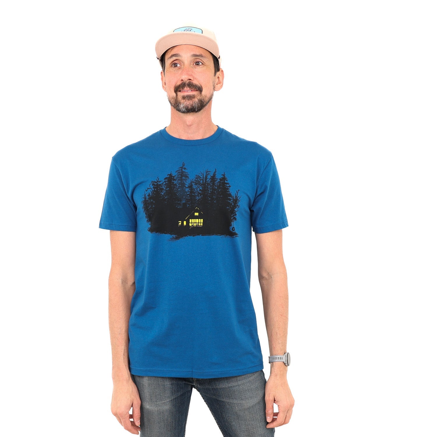 Man wearing blue t-shirt with print of black ink of silhouetted trees with yellow ink house lights shining out of darkness. Two animals sitting in the window.