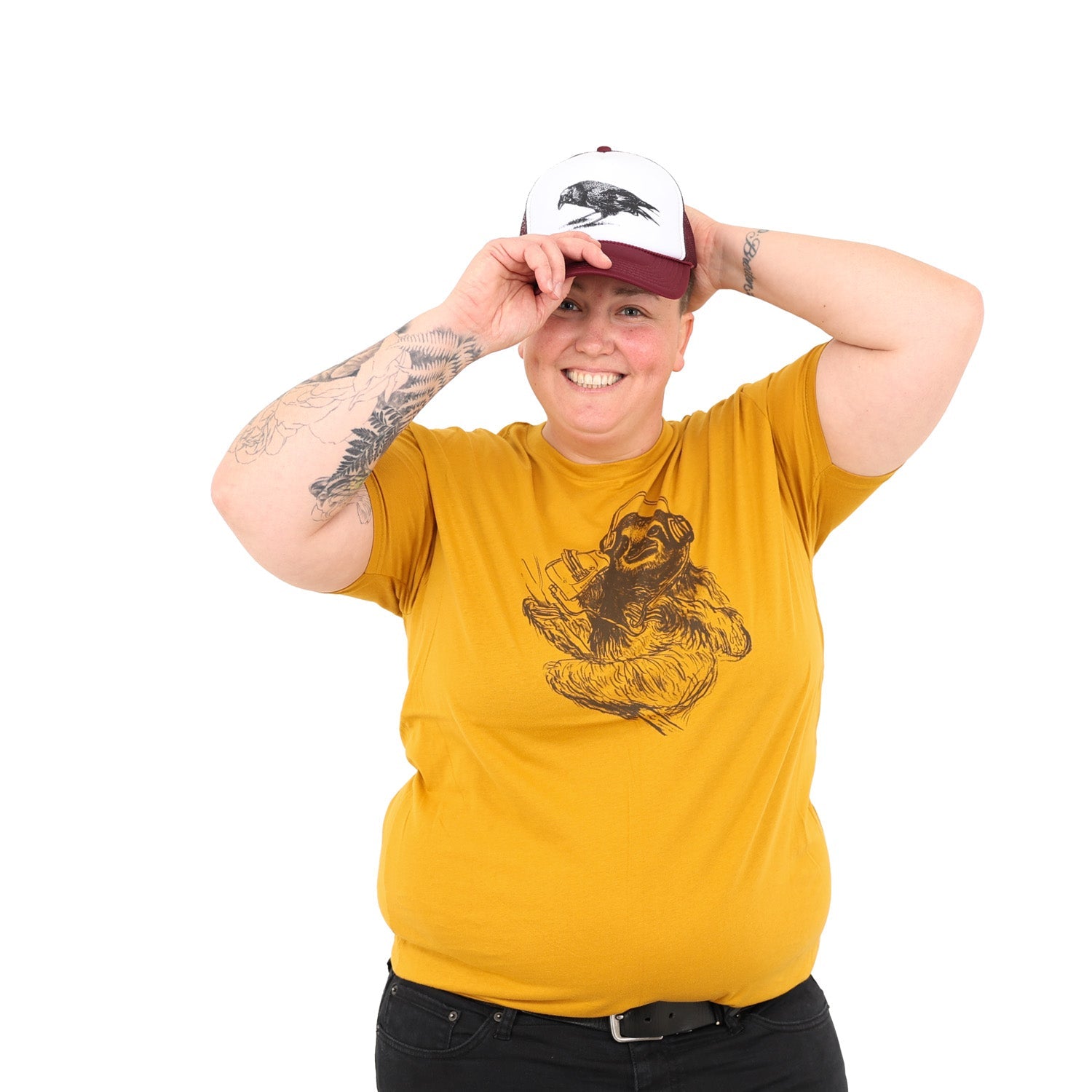 girl putting a hat on while wearing a mustard yellow shirt with a brown screen print of a sloth listening to music on headphones.