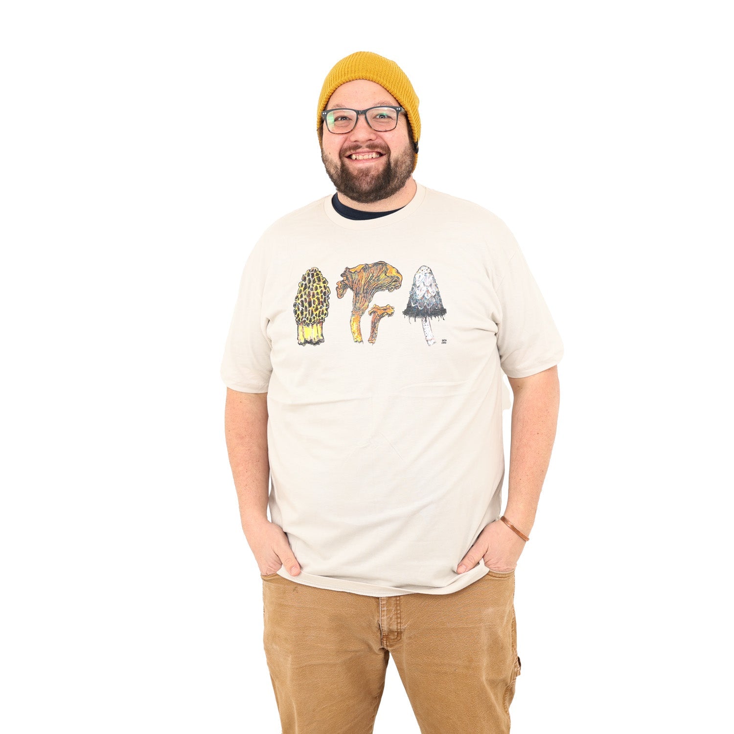 man wearing a tan colored shirt with three mushrooms- morel, chantrelle, and shaggy mane