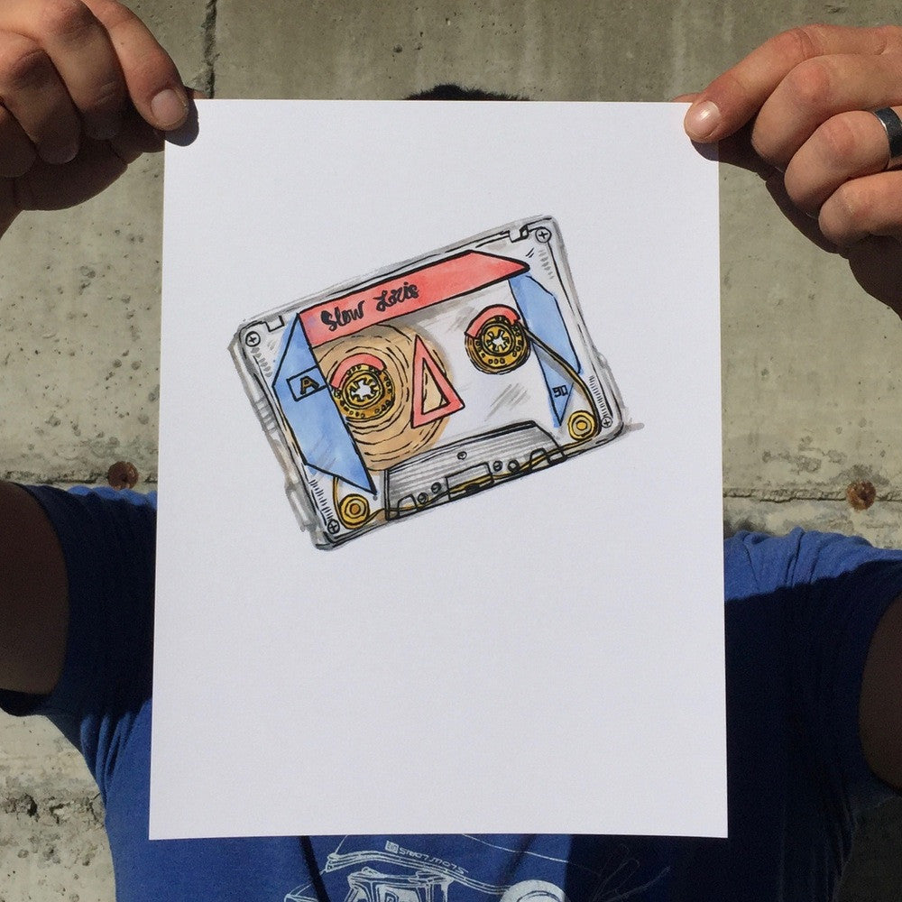 Art print of colorful cassette tape against white background, held up by pinched fingers at top corners