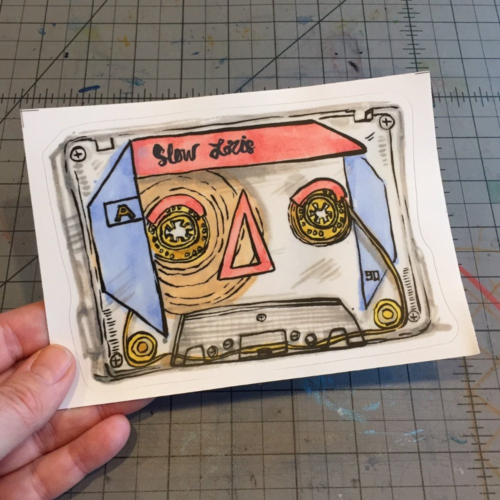 Sticker of a colorful 90s cassette tape, in hand.