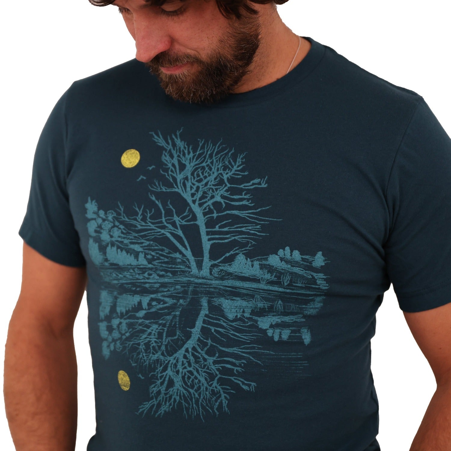 Man wearing atlantic blue t-shirt. Print is in a light blue tree & reflection over water with a yellow moon.