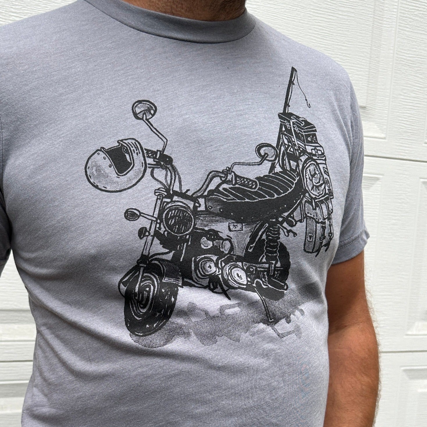 Black print on a grey colored t-shirt. Print is of a mini-bike loaded up with fishing pole, helmet, sleeping bag, and bags.