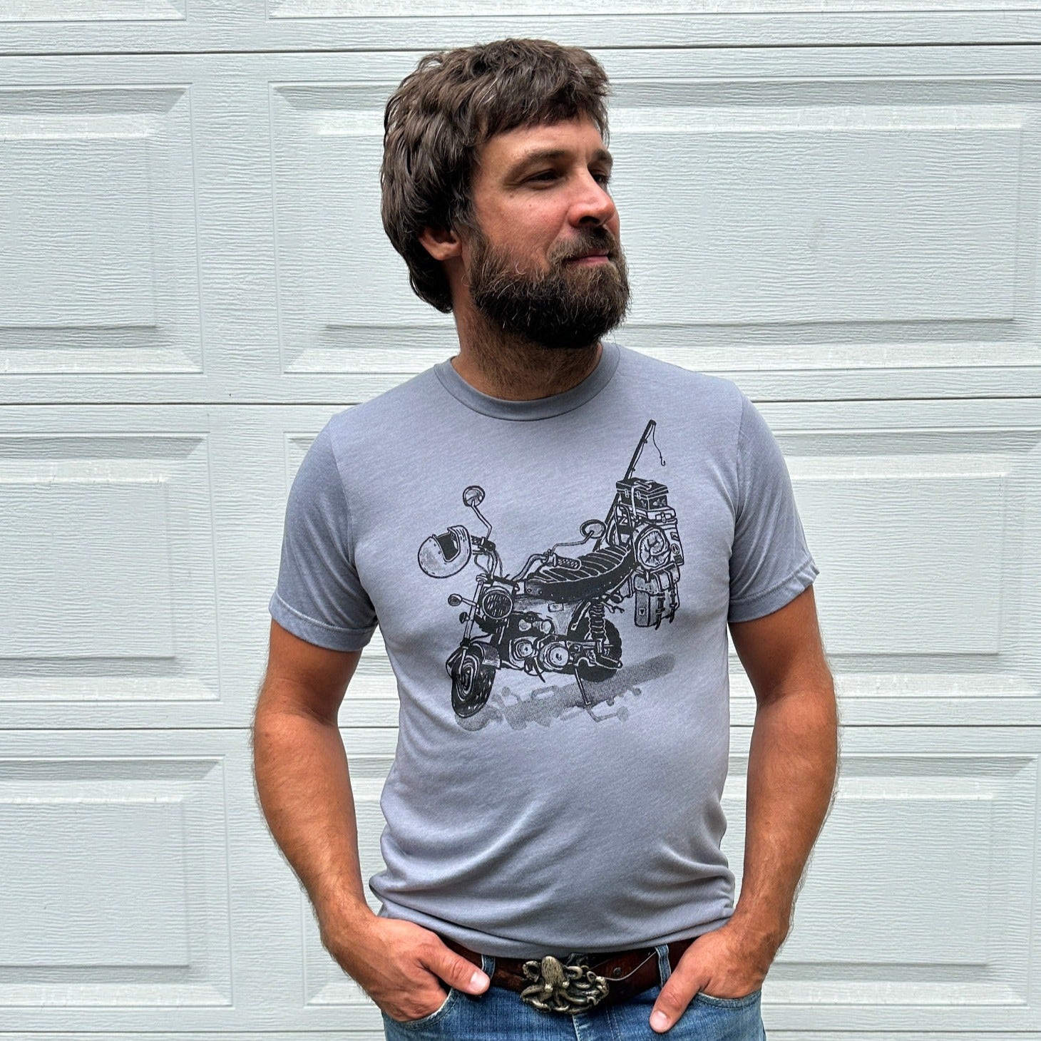 Black print on a grey colored t-shirt. Print is of a mini-bike loaded up with fishing pole, helmet, sleeping bag, and bags.