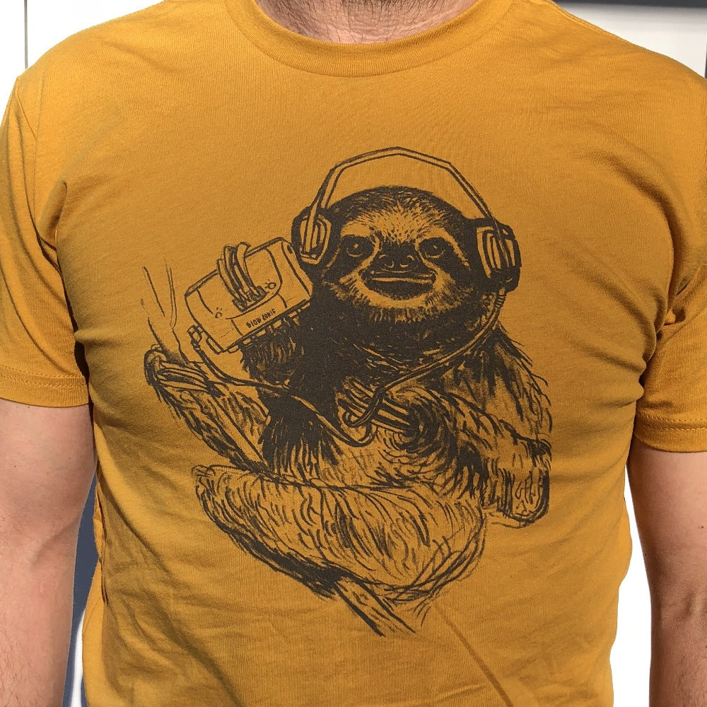 close up of man wearing a mustard yellow shirt with a brown screen print of a sloth listening to music on headphones.