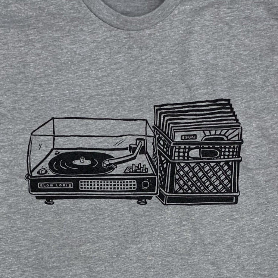 Close up of light grey shirt with black print of a record player with a milk crate full of records next to it.