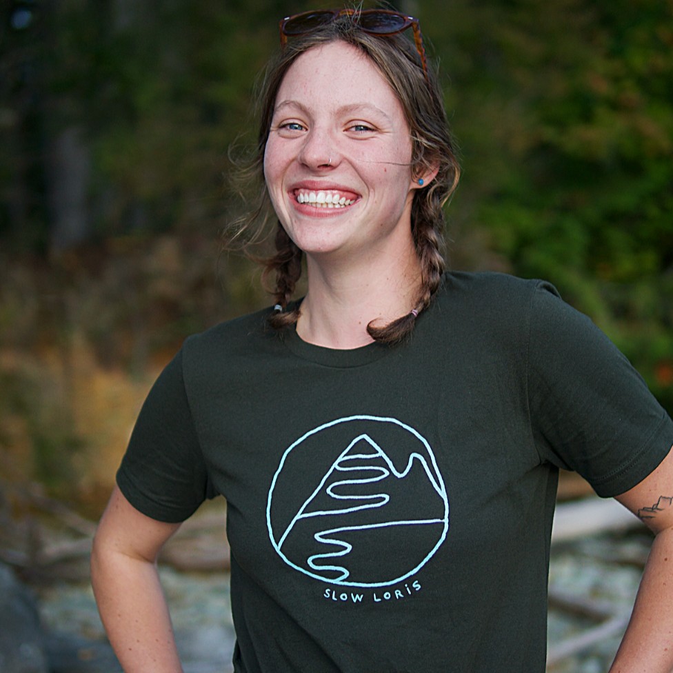 smiling woman wearing dark green t-shirt with light blue print of mountain hug.