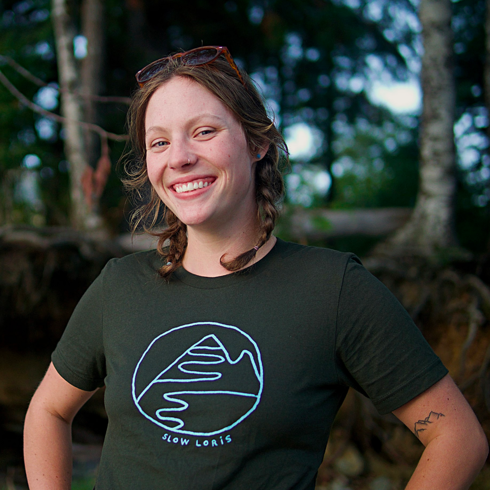 smiling woman wearing dark green t-shirt with light blue print of mountain hug.