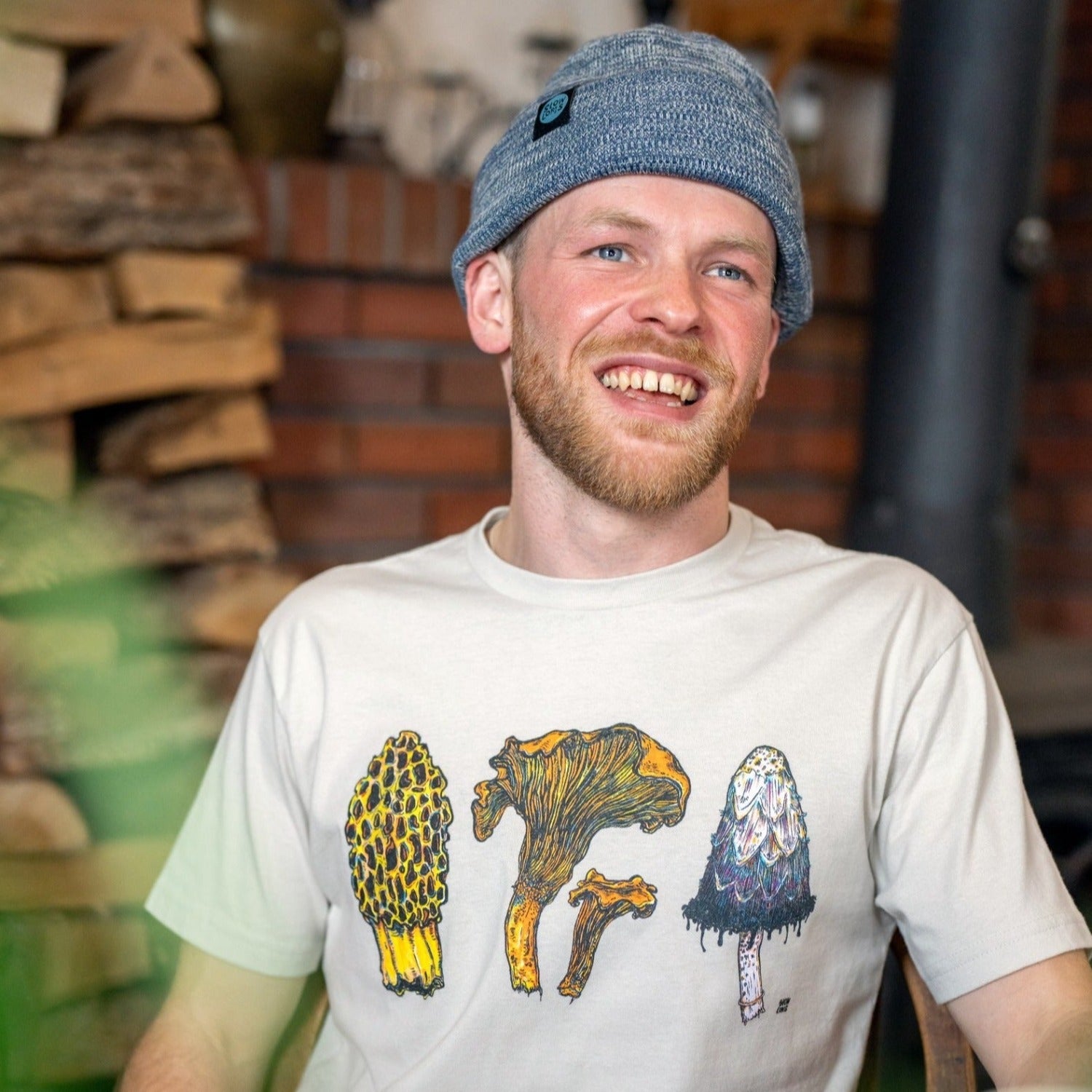 man wearing a tan colored shirt with three mushrooms- morel, chantrelle, and shaggy mane