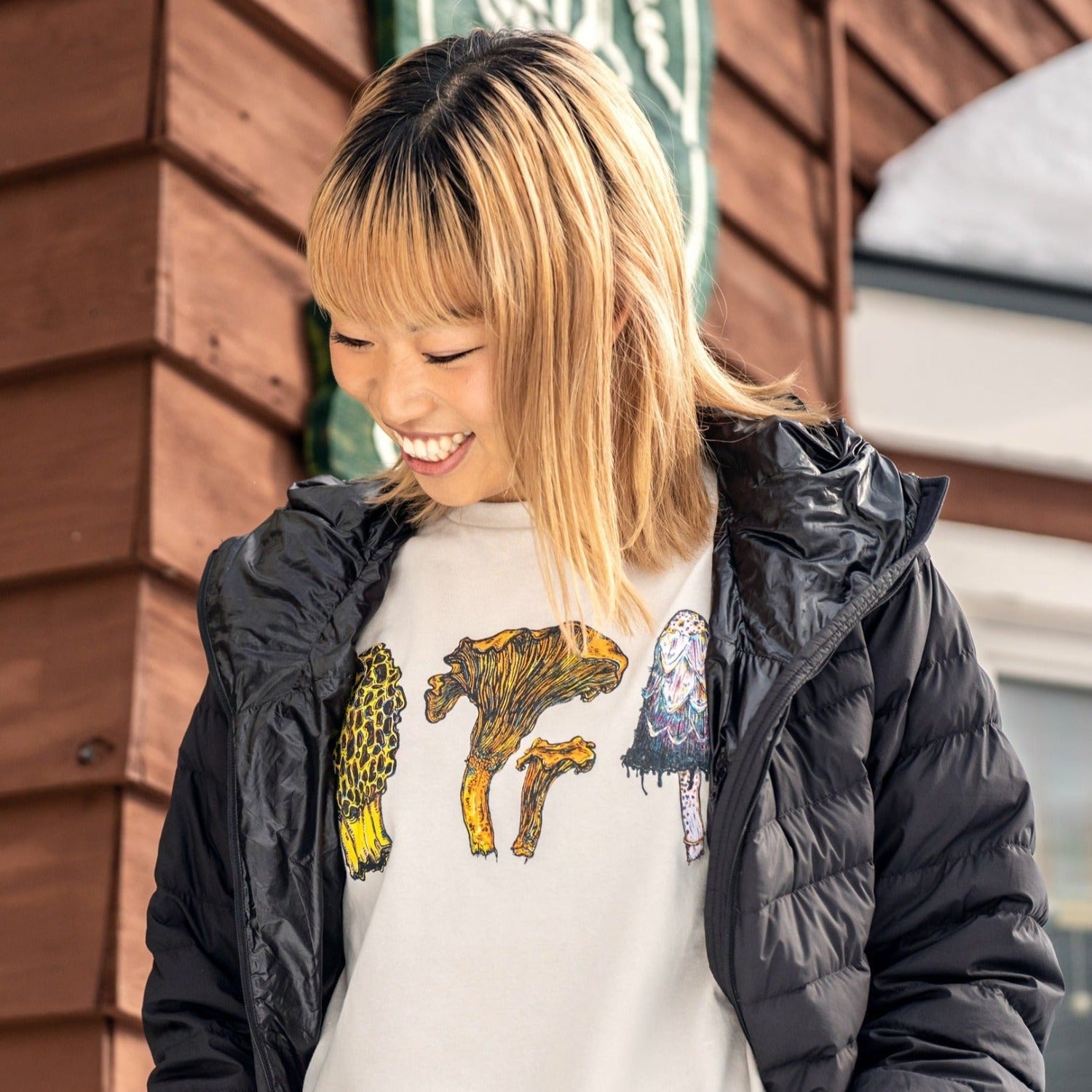 woman wearing a tan colored shirt with three mushrooms- morel, chantrelle, and shaggy mane