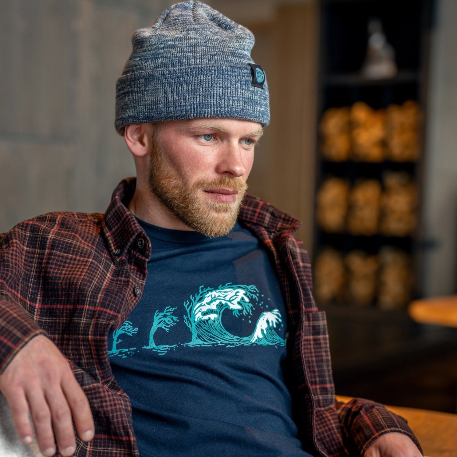 Man looking off into distance while wearing a dark blue shirt with trees turning into waves in white and light blue ink