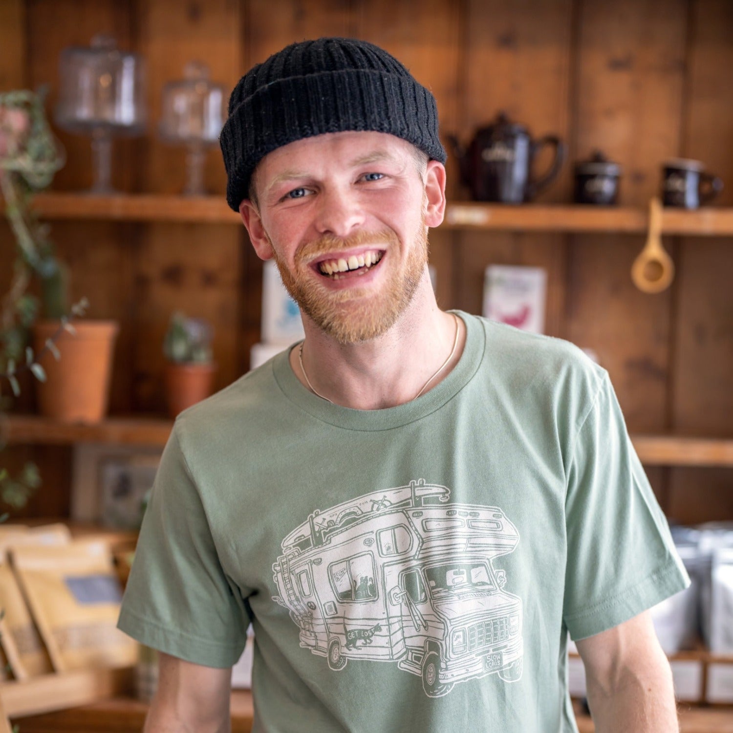 man inside wearing black beaning and a light green shirt with a loaded up RV on it. .