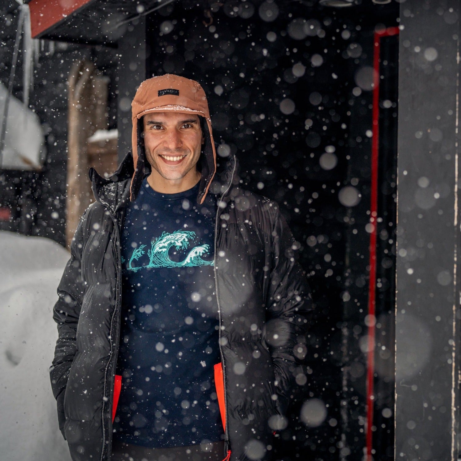 man standing in snow while wearing a dark blue shirt with trees turning into waves in white and light blue ink