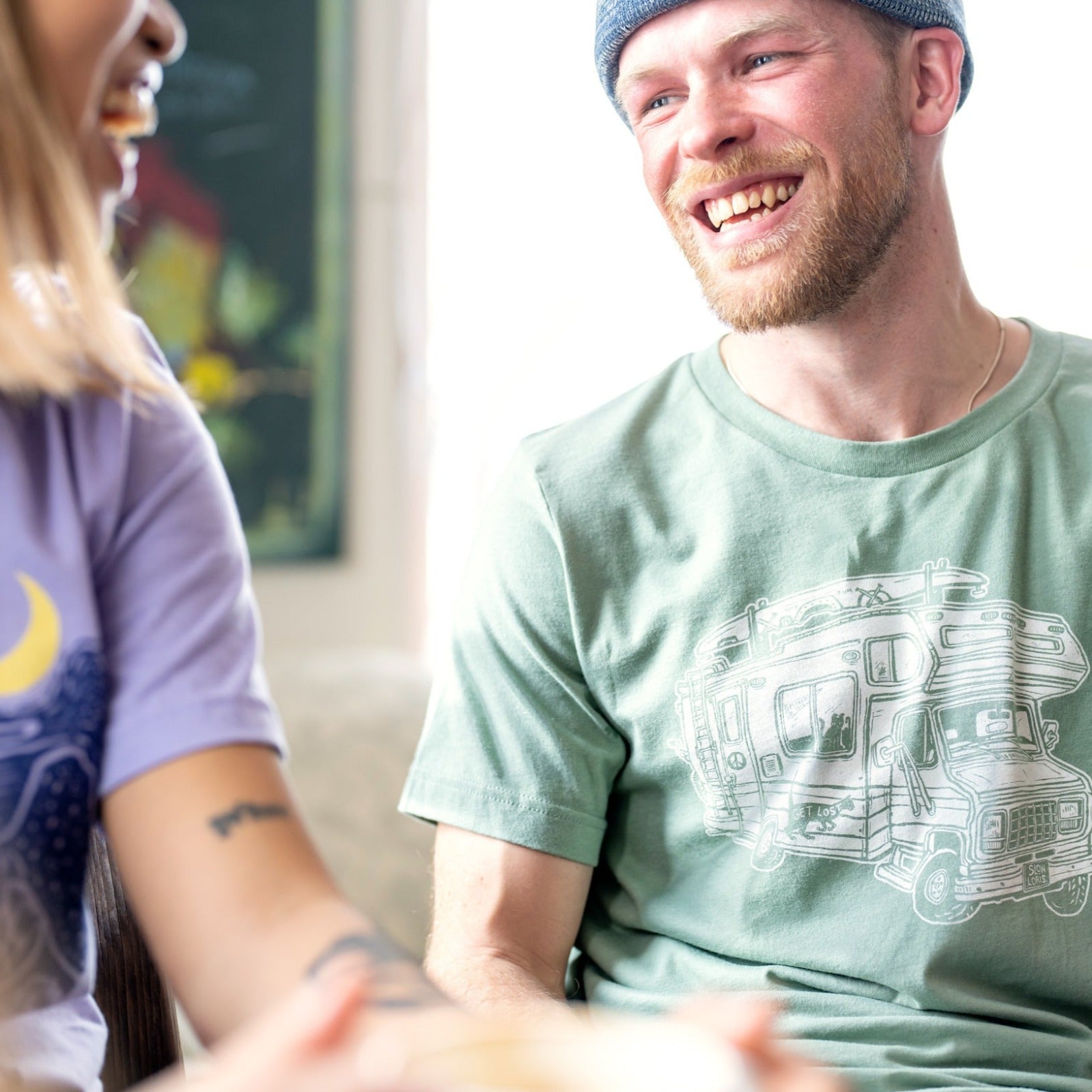 Man smiling at a girl while wearing a light green shirt with a loaded up RV on it. .