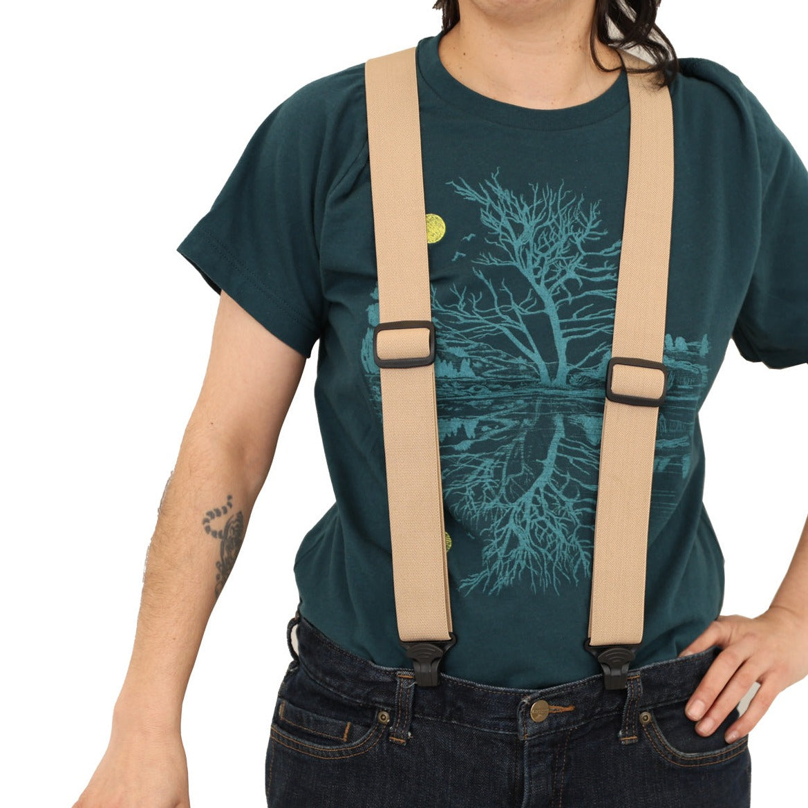 Woman wearing atlantic blue t-shirt with suspenders and a hat in her hands. Print is in a light blue tree & reflection over water with a yellow moon.