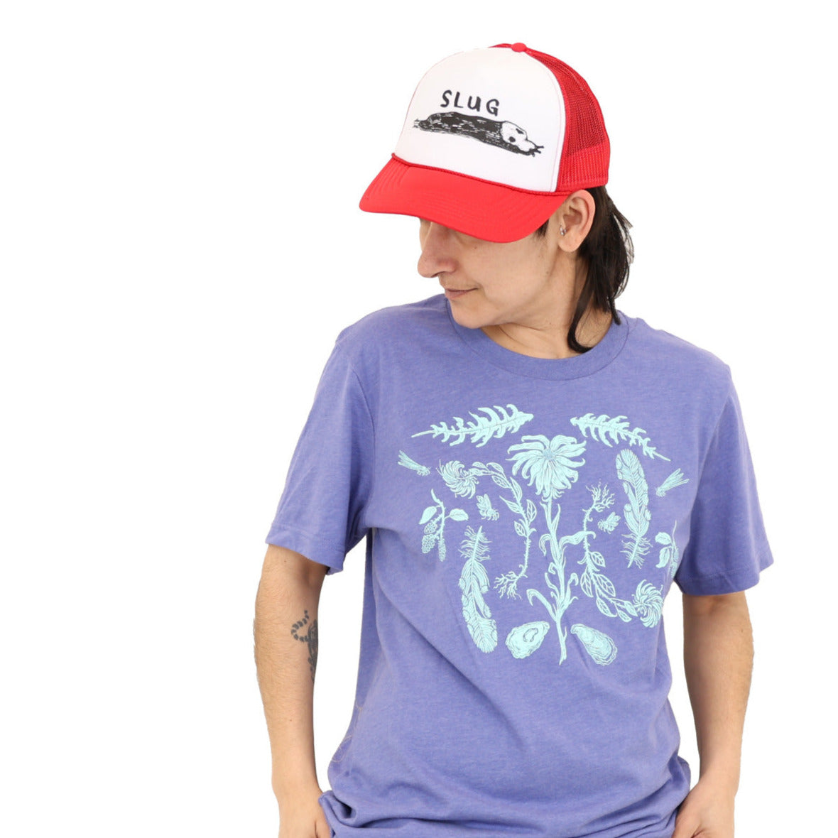 Woman wearing a light purple colored t-shirt with light blue ink of flowers, ferns, feathers, shells, etc