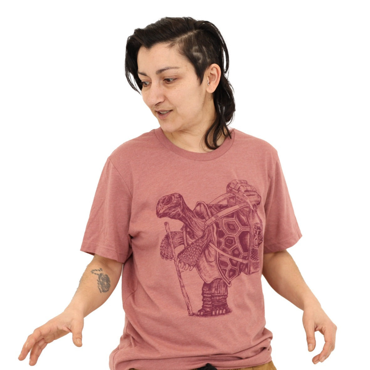 Woman wearing a mauve shirt with darker mauve ink of a hiking tortoise.