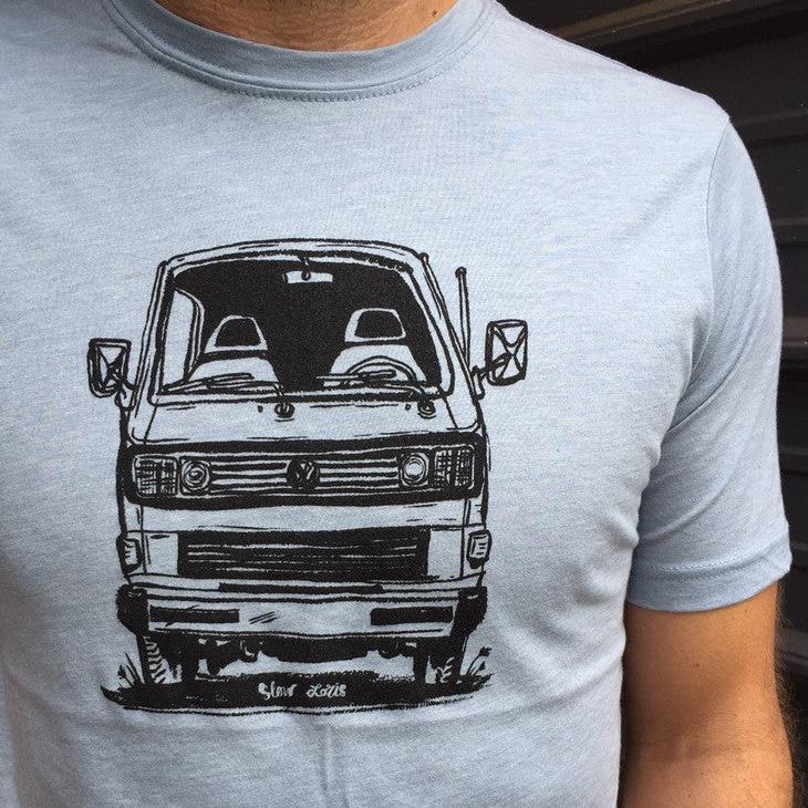 Man wearing light blue t-shirt with black print of face on view of VW van
