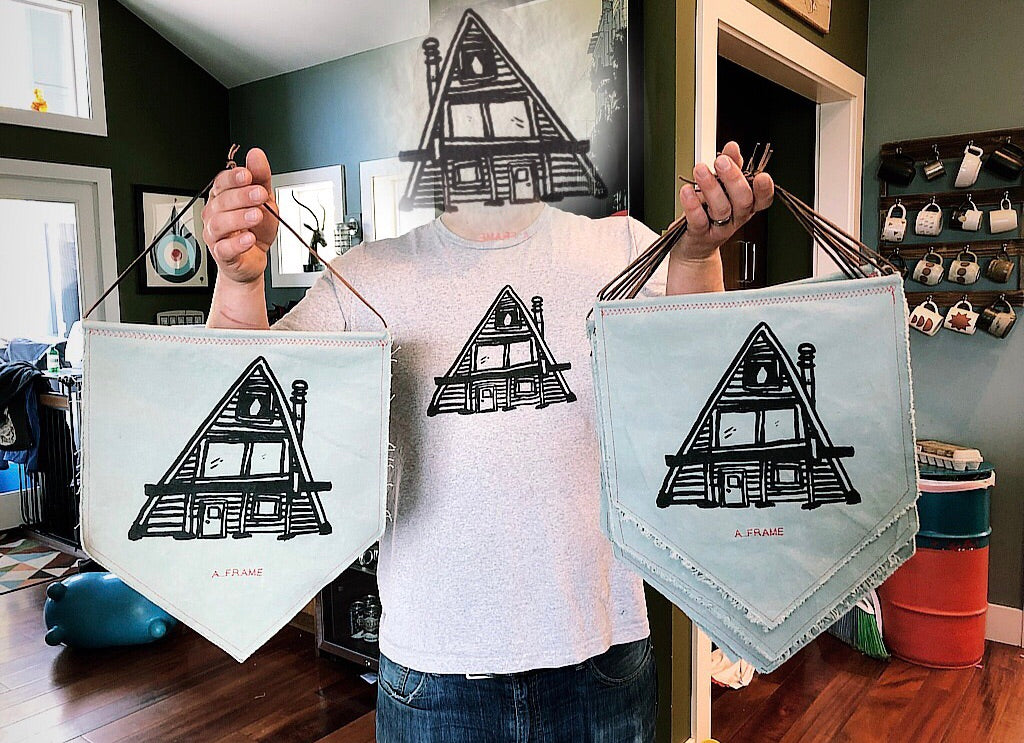 A-Frame wall art pennants held by man with A-Frame for a head, wearing an A-Frame t shirt 
