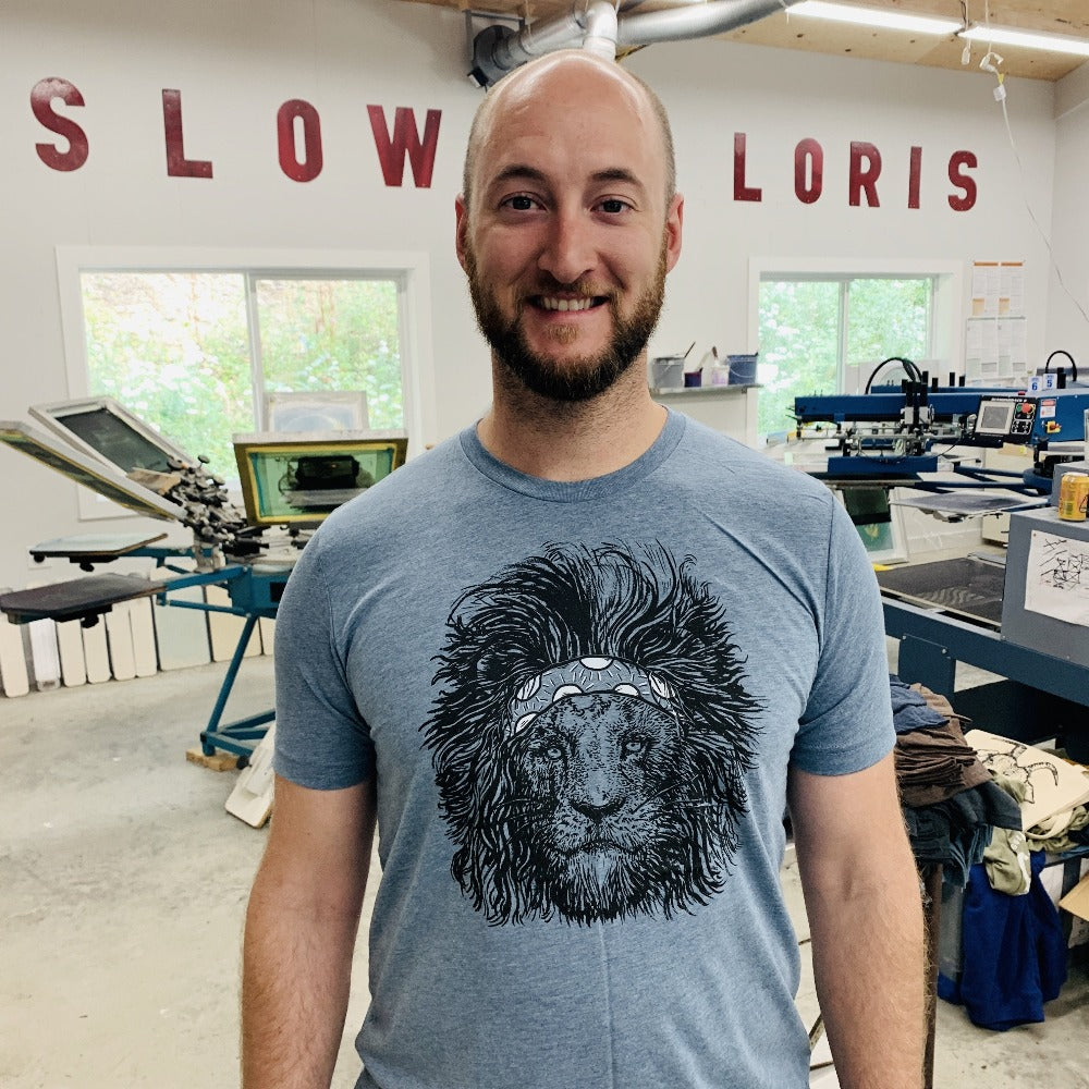Cliff in the shop wearing a steel blue tee with a screen printed lion wearing a headband on it.