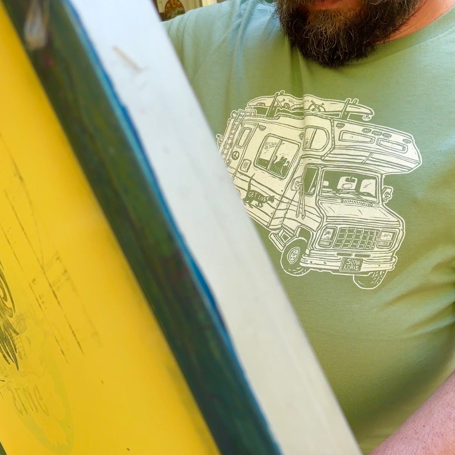 Man holding up a screen while wearing a light green shirt with a loaded up RV on it.