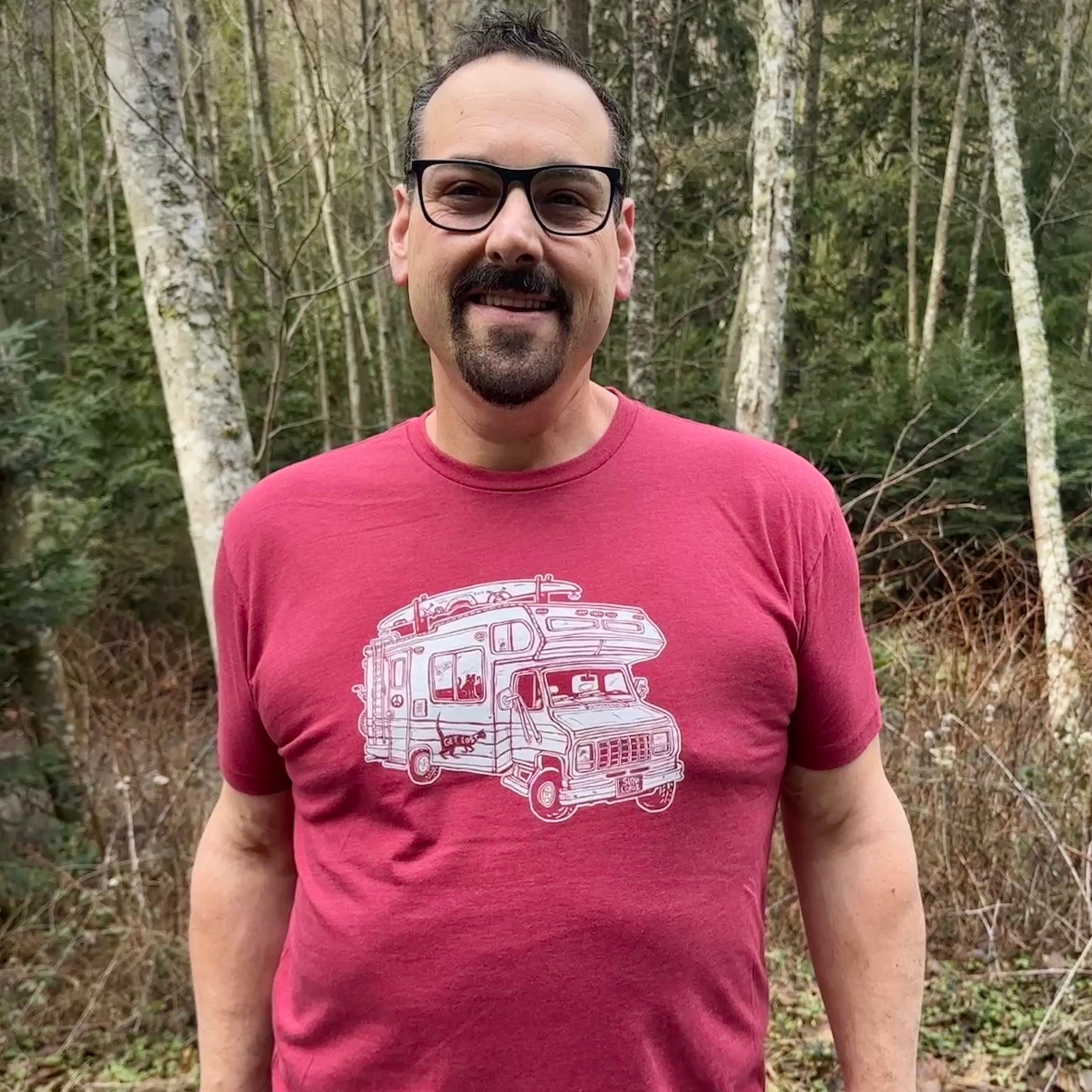 Man standing outside wearing a red shirt with a loaded up RV on it. .