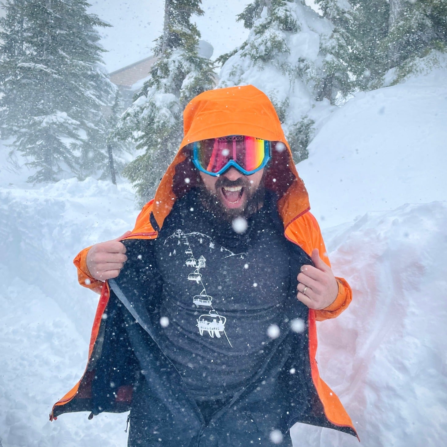 Smiling man in snowstorm, opening snowsuit to reveal t shirt printed with chairlift.