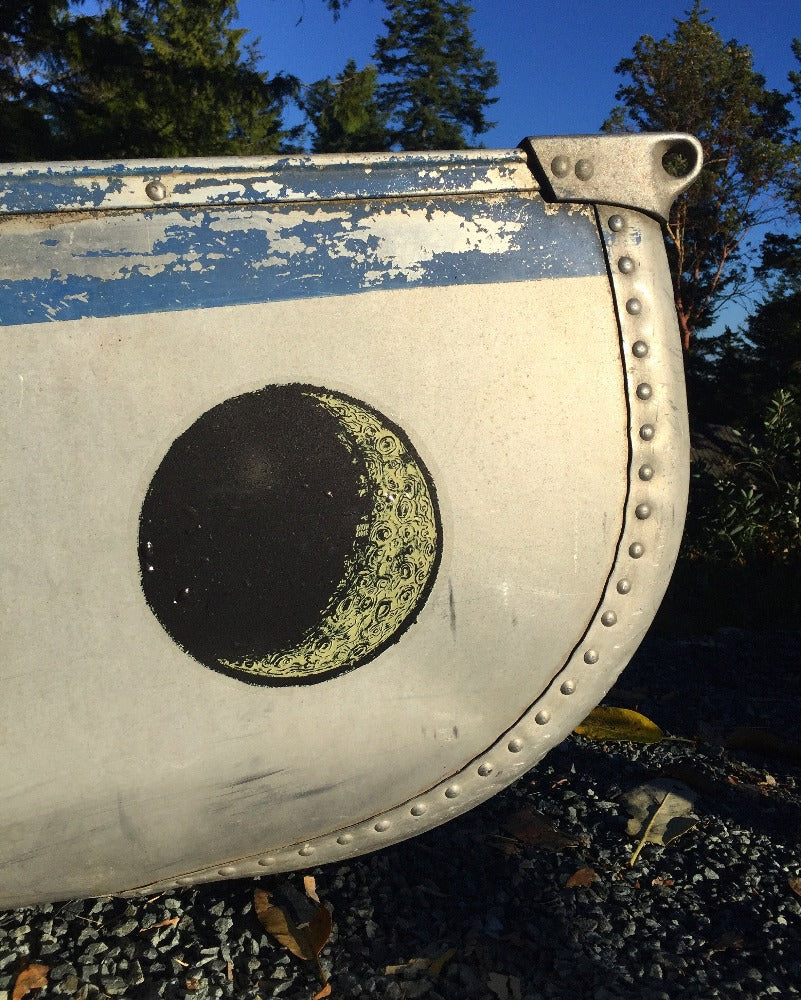 A large vinyl "stained glass" sticker in the shape of the waxing crescent moon, stuck to the bow of a canoe.