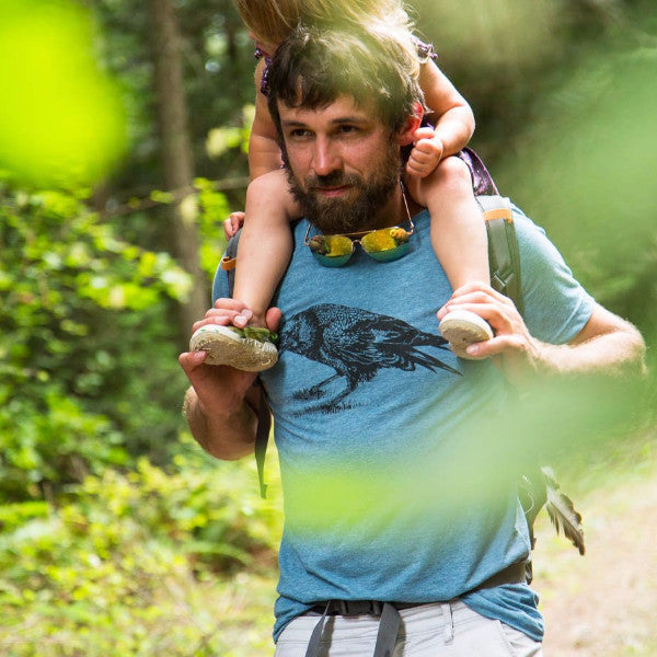 Blue t shirt screen printed with a black crow, worn by a man hiking with his daughter on his shoulders.