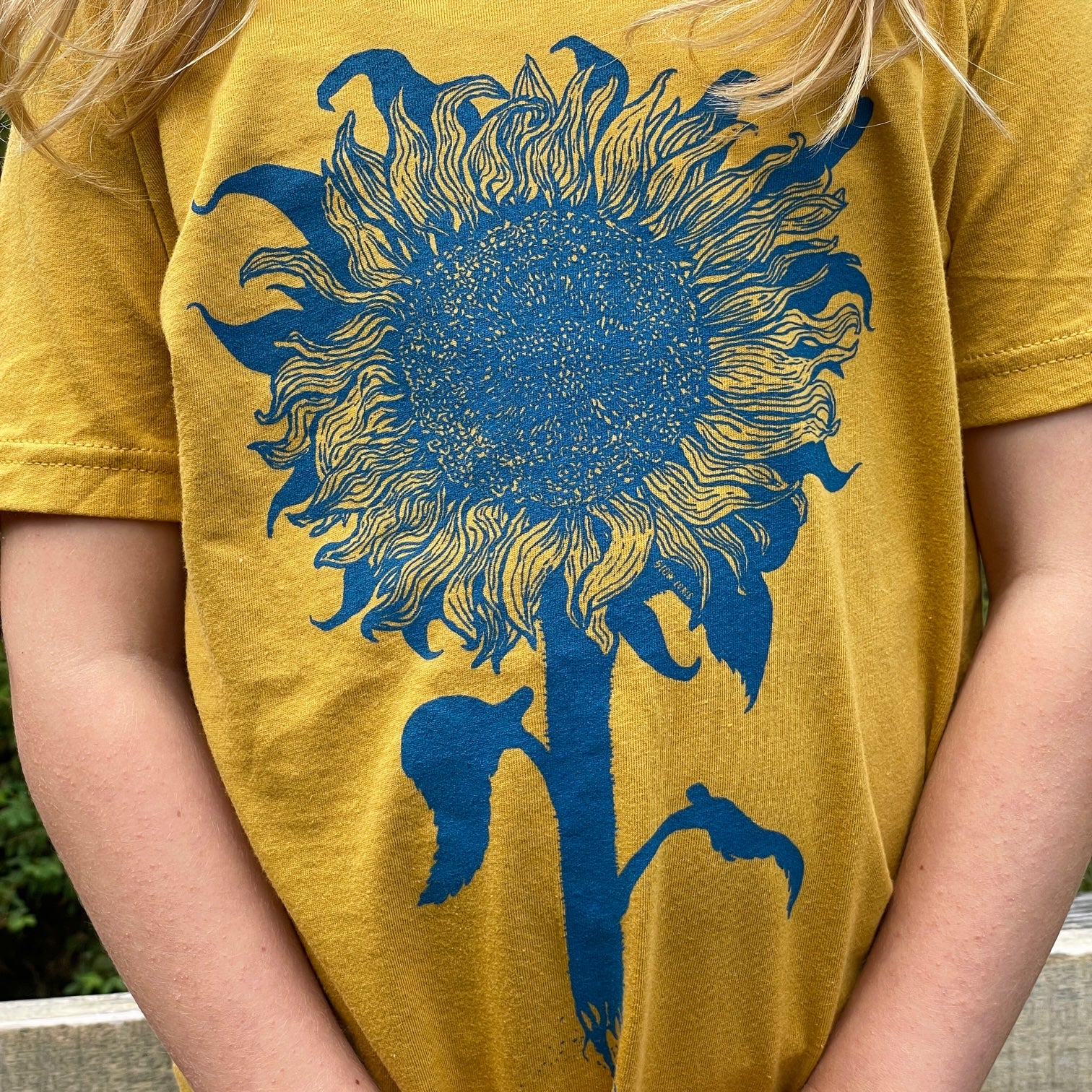 close up of a mustard colored t-shirt with light blue print of an intricate sunflower.