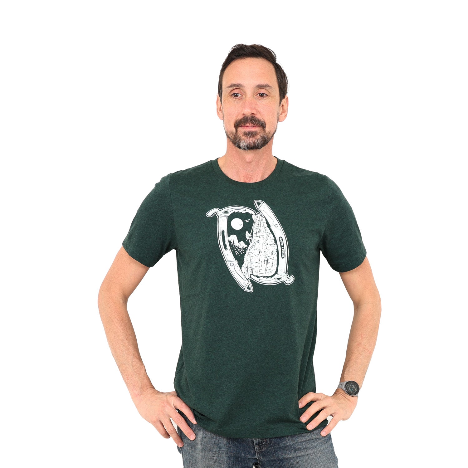 Man standing with hands on his hips with a whitebackground while wearing a green t-shirt with ice Axes framing a climbing scene.