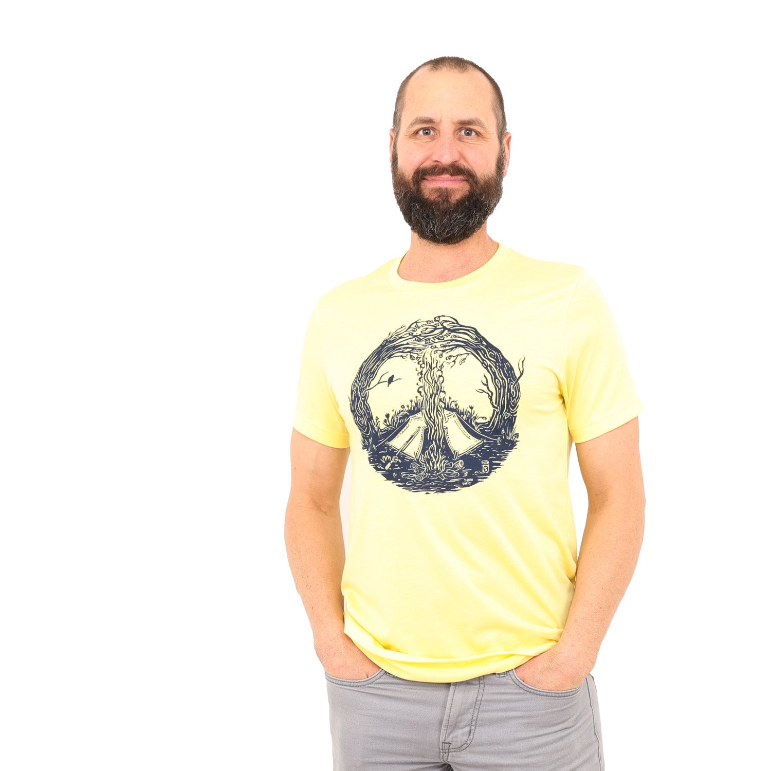 Man wearing yellow t-shirt with print is of a campfire's smoke going up the center meeting with the tops of curved in trees creating a peace sign. Tent is by the fire and a bird is on a branch