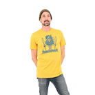 Man wearing beanie and mustard yellow t-shirt with a tree dude standing on a canoe with paddles in his outstretched hands