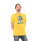 Man wearing beanie and mustard yellow t-shirt with a tree dude standing on a canoe with paddles in his outstretched hands