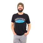 Man wearing a beanie in grey jeans and a black t-shirt with a blue mountain and white wind lines screenprinted