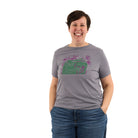 woman wearing a hat and a slow loris grey t shirt with pink/purple plants and green radio
