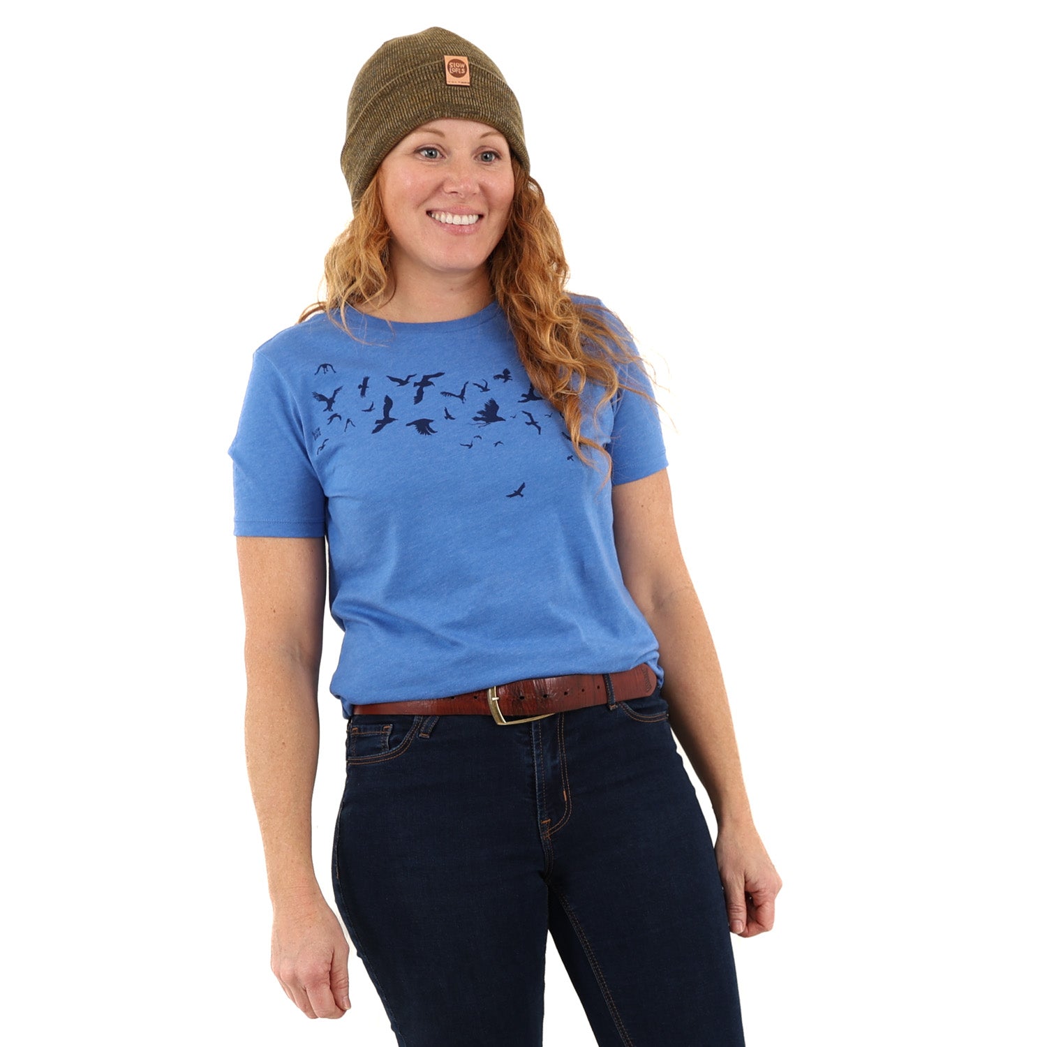 woman wearing green/brown beanie with blue t-shirt with dark blue ink of birds flying.