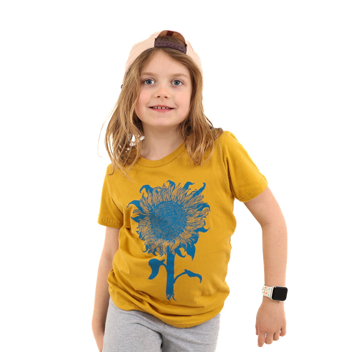 Little girl wearing a mustard colored t-shirt with light blue print of an intricate sunflower.