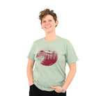 Smiling woman wearing soft green t-shirt with maroon red print of a lookout tower in the mountains. 