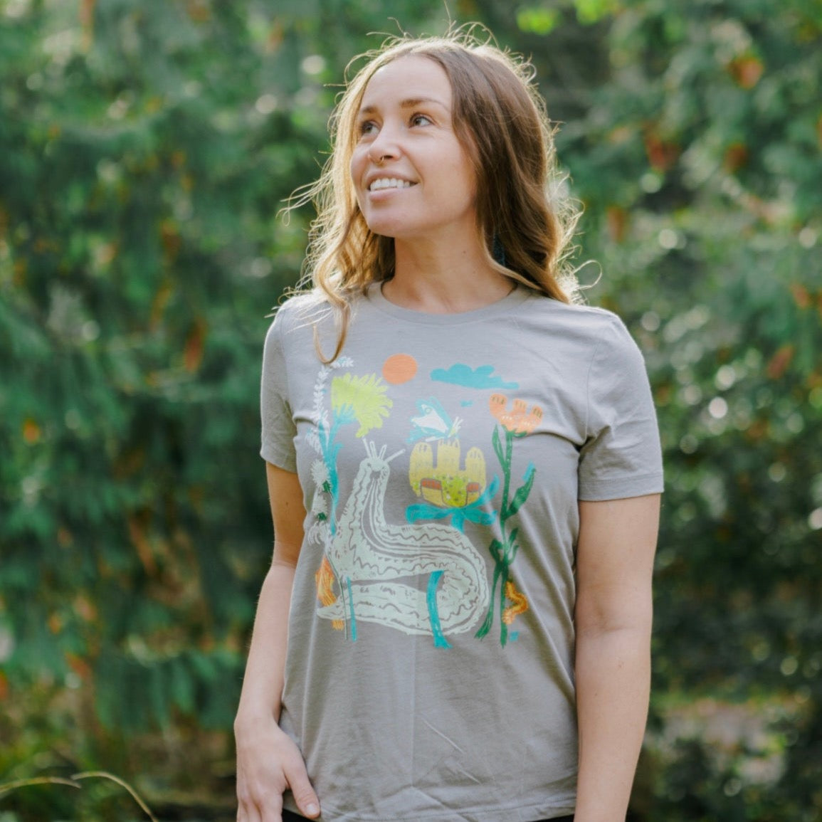 Woman wearing light brown t shirt with colorful print of plants and bugs -